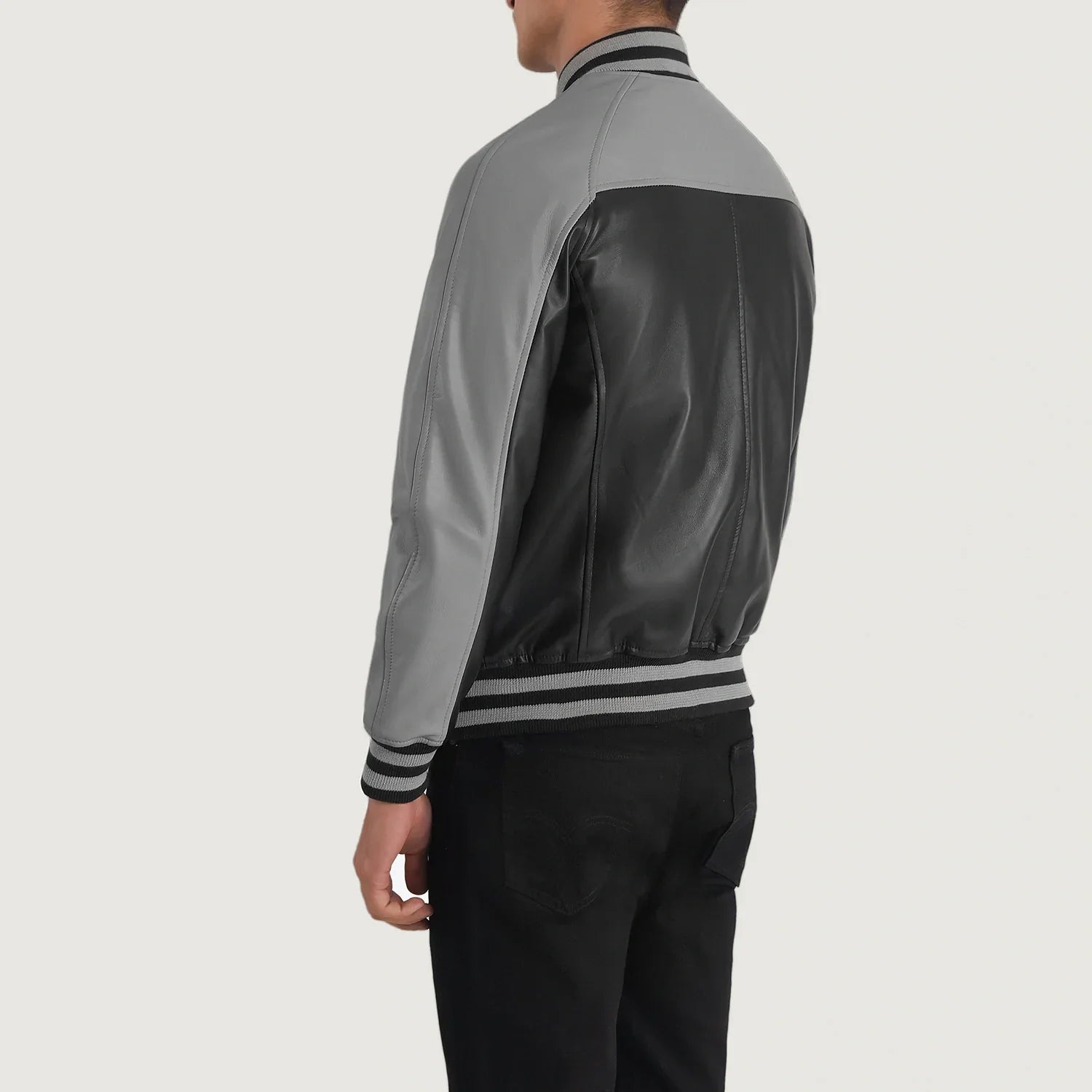 Back view of a black and grey leather varsity jacket worn by a male model with striped collar and cuffs
